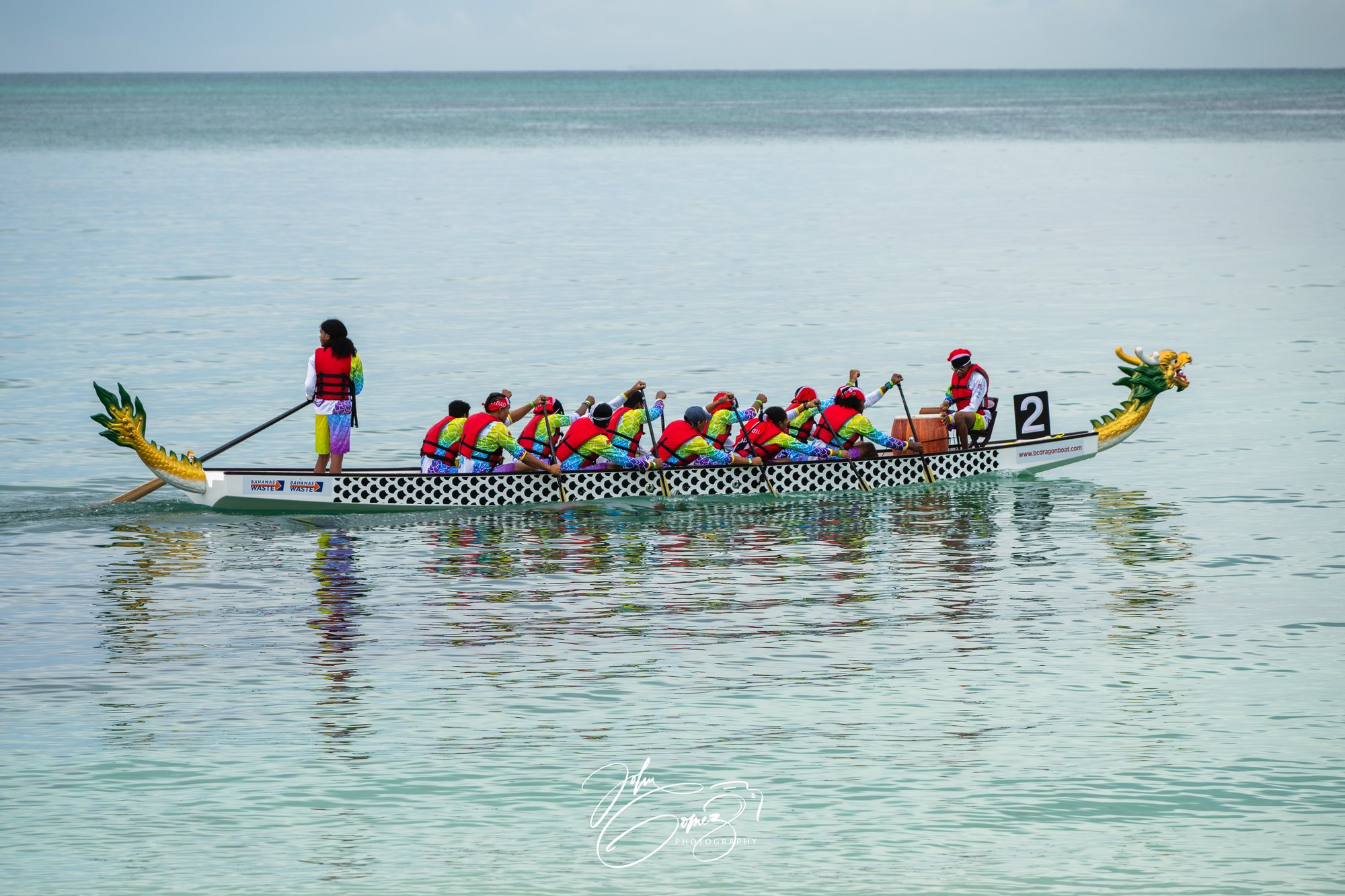 A dragon boat crew paddling out across flat water off Goodman's Bay
